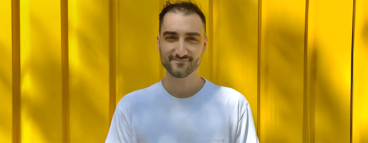 A photo of Matt Bonacini wearing a white t-shirt in front of a yellow background